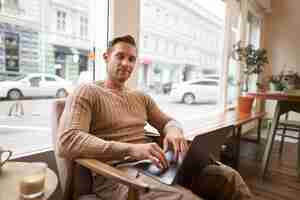 Free photo portrait of young working professional man sitting in cafe with laptop drinking coffee and working