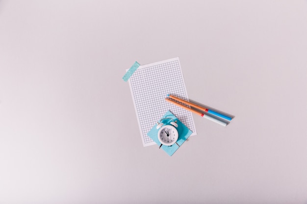 portraits of alarm clock lying on sheet of paper glued to white table.