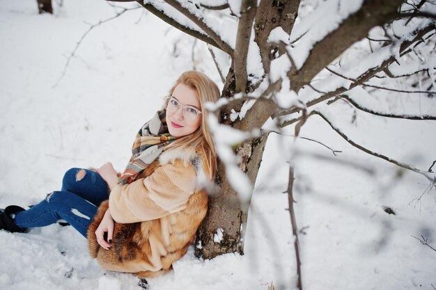 Portraiy of blonde girl in glasses red fur coat and scarf at winter day