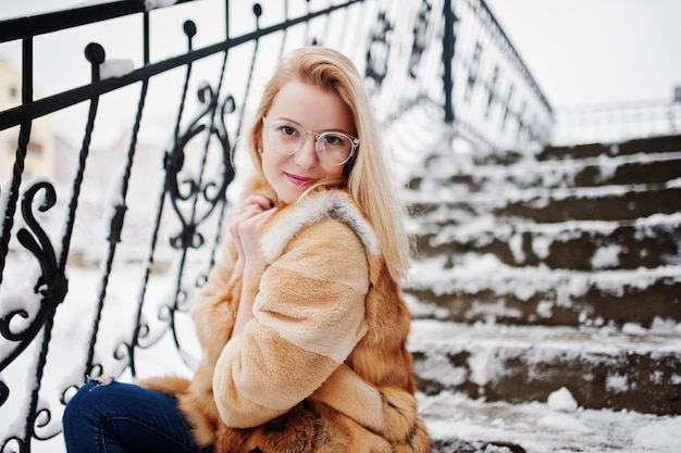 Portraiy of blonde girl in glasses red fur coat and scarf at winter day