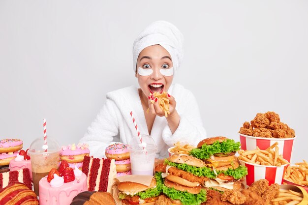 Positive Asian female model eats french fries consumes junk food 