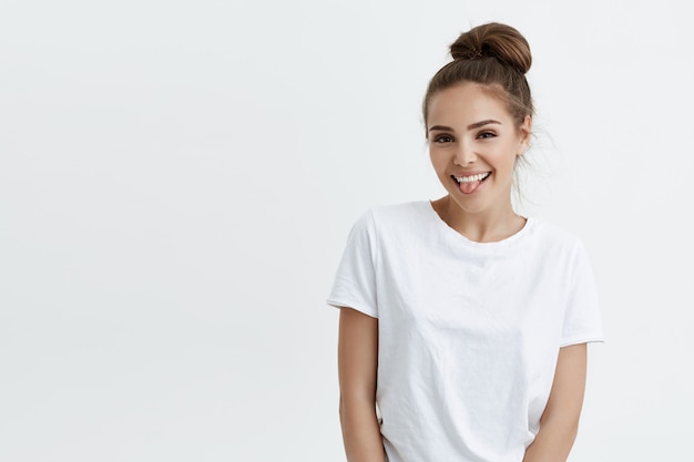 Positive attractive caucasian woman with bun, sticking out tongue and smiling, looking glad and pleased