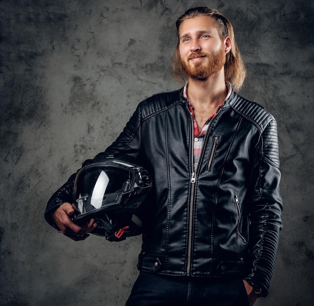 Free Photo positive bearded redhead male in leather jacket holds motorcycle helmet on grey background.