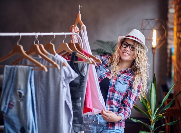 Free Photo positive blonde female in black eyeglasses chooses fashionable clothes on the coat rack.