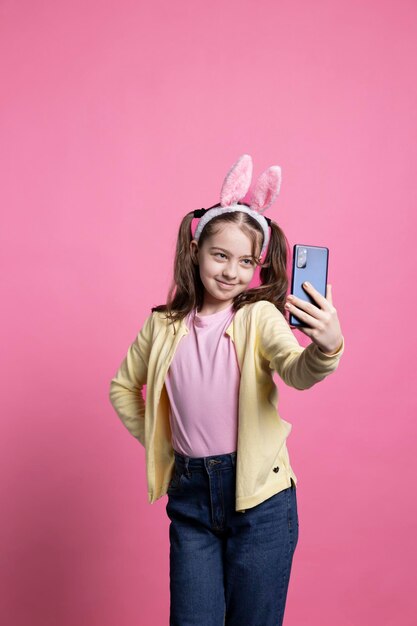 Positive cute schoolgirl taking pictures with her mobile phone in studio