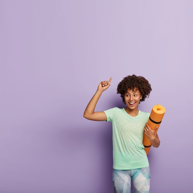 Free photo positive dark skinned female with afro hairstyle, wears casual t shirt and leggings, has fitness meditation