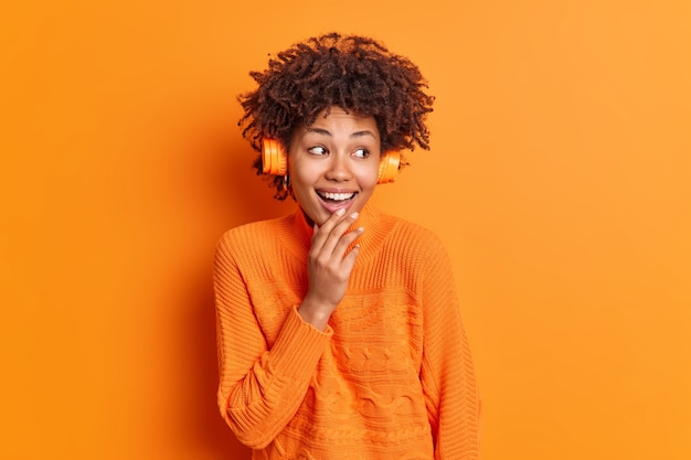 Positive dark skinned young woman with curly hair listens audio track