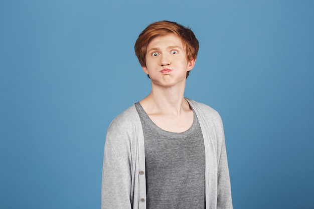 Positive emotions. Close up portrait of young good-looking ginger guy in stylish grey t-shirt under casual cardigan  with foolish face expression, having fun.