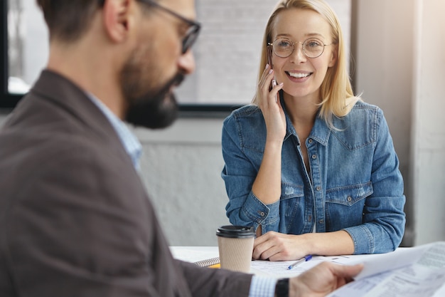 Positive female assistant and bearded serious male entrepreneur in office