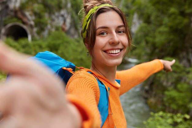 Free photo positive female blogger shoots video online while explores nature, points into distance