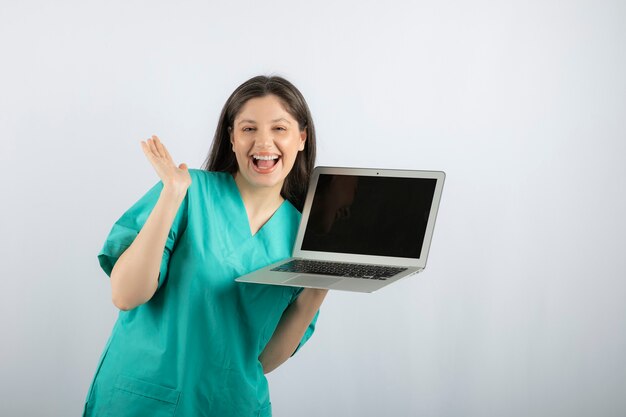 Positive female nurse posing with laptop on white. 