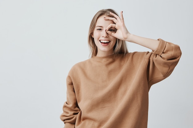 Positive funny blonde woman in casual clothes shows ok sign