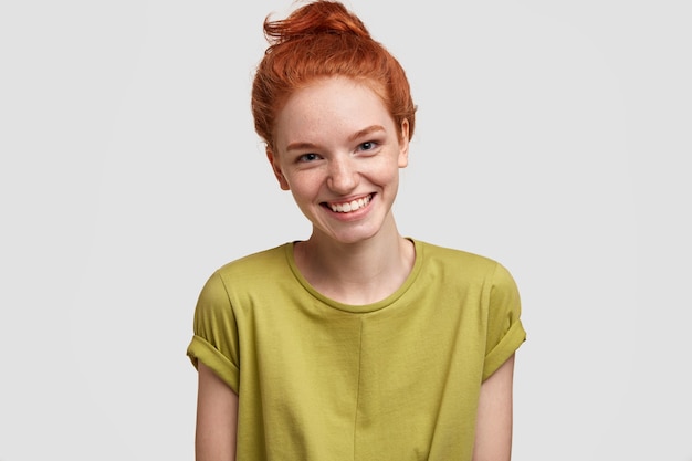 Free Photo positive ginger femae with freckled skin, broad smile, dressed in casual green t shirt, isolated over white wall