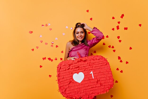 Positive girl posing with internet banner. Glad brunette woman standing on yellow with red confetti.