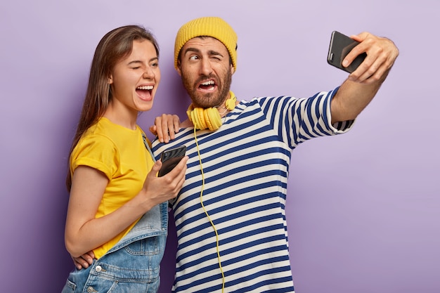 Free photo positive guy and female blink eyes, pose in front of cell phone camera, make photo for internet blog, take selfie, have glad expressions