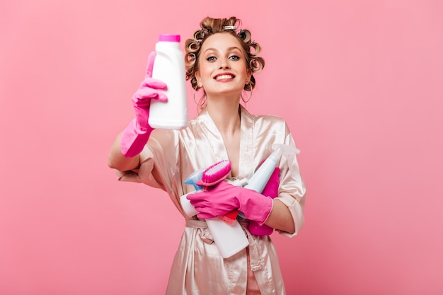 Positive housewife in silk outfit holds brushes and detergents