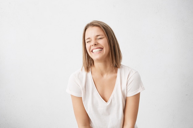 Positive human emotions. Headshot of happy emotional teenage girl with bob haircut laughing from the bottom of her heart, keeping eyes closed, showing perfect white teeth while having fun indoors