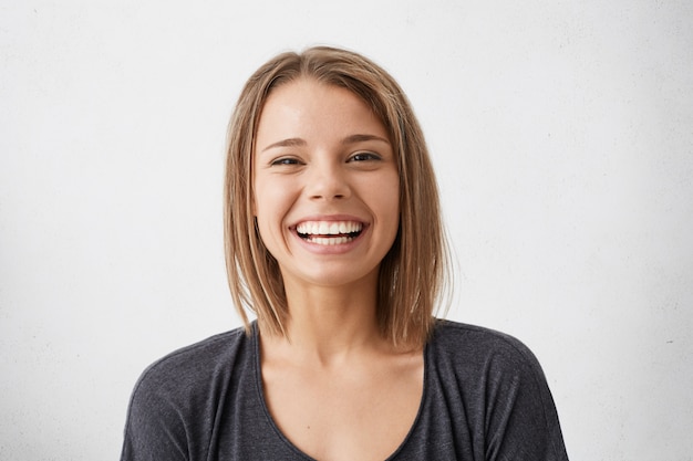 Free photo positive human facial expressions and emotions. cheerful attractive teenage girl with bob hairstyle grinning broadly, showing her perfect white teeth while spending nice time indoors