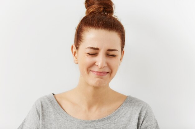 Positive human facial expressions, emotions and feelings. Portrait of funny beautiful redhead European teenage woman dressed in grey t-shirt closing her eyes and pursuing lips, can't stop laughing