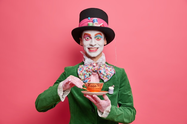 Free Photo positive male hatter enjoys tea party dressed in hat and green velvet jacket poses against rosy wall looks like real gentleman