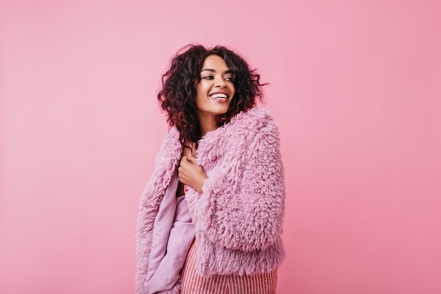 Positive, smiling brunette in pink outfit looks joyfully into distance. Portrait of girl with tanned skin .