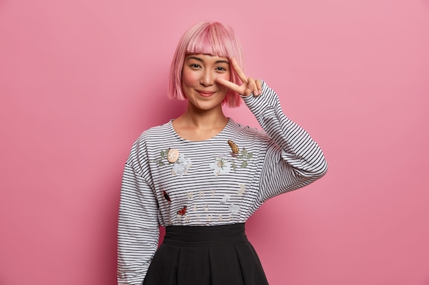 Free Photo positive smiling pink haired girl shows peace sign, wears striped jumper and black skirt