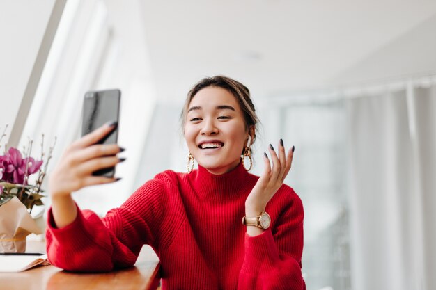 Positive woman in bright sweater laughs and talks on video in phone