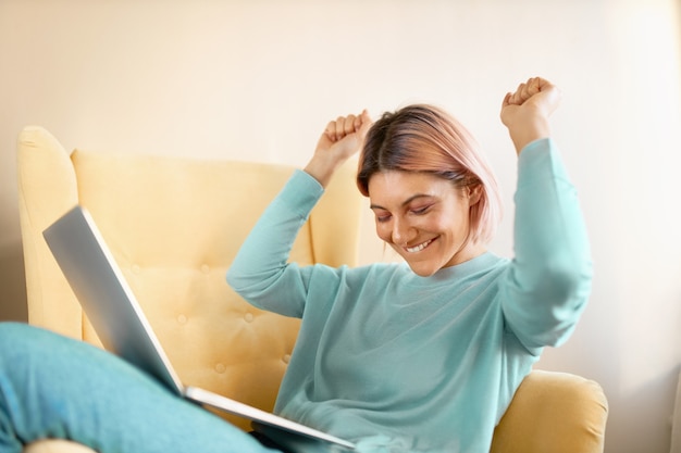 Positive woman win a prize in  the internet and try to dancing on the chair.