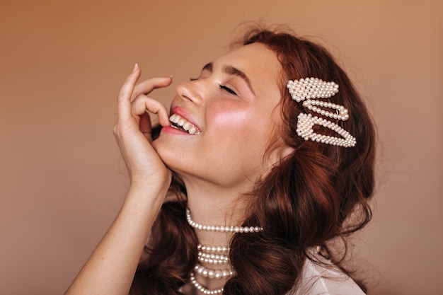 Free Photo positive woman with curly hair laughs and bites her finger. portrait of woman with white hairpins and pearl necklace.