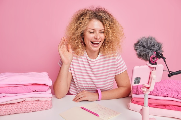 Free photo positive woman with curly hair waves hello at camera