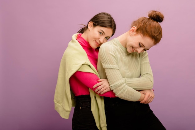 Free Photo positive young caucasian brunette girl in casual clothes will hug her redhaired girlfriend on purple background people sincere emotions lifestyle concept