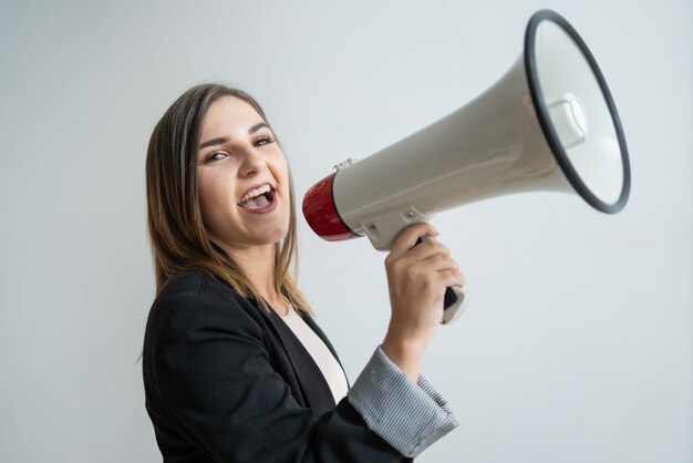 Positive young Caucasian woman shouting in raised megaphone