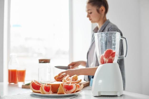 Free photo positive young girl cutting grapefruit blending healthy detox fresh smoothie over white wall.