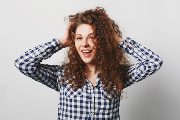 Free photo posittive woman shows her bushy curly hair, wears casual checkered shirt, isolated over white