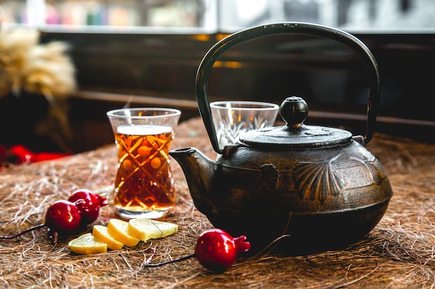 Free photo pot of tea with glass and lemon side view