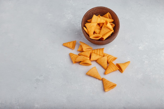 Potato chips spread over the white surface out of the wooden bowl. 