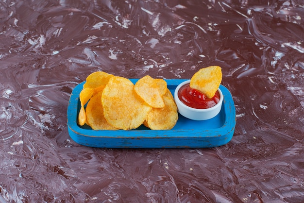 Potato chips with ketchup in a wooden plate , on the marble table. 