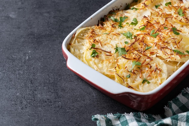 Potato gratin baked with cream and cheese on black slate background