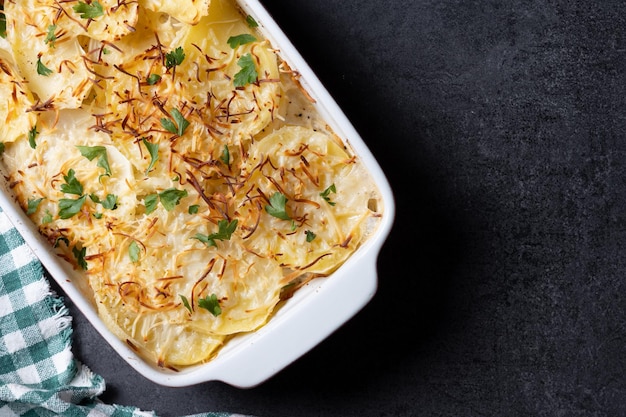 Potato gratin baked with cream and cheese on black slate background