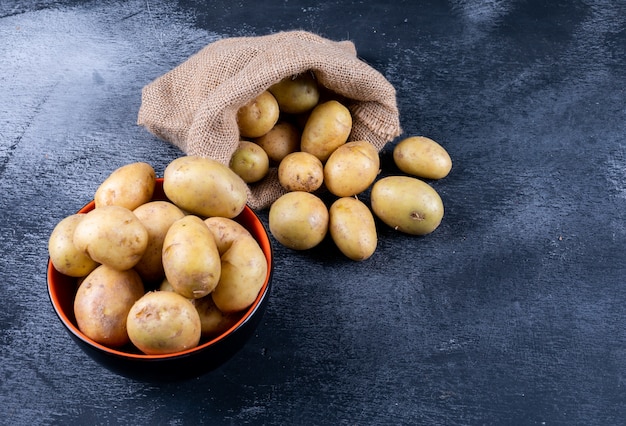 Free photo potatoes in a sack bag and bowl on a dark table