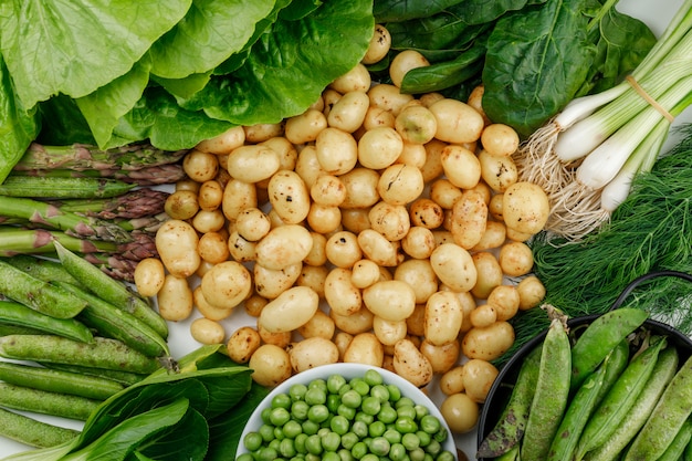 Potatoes with green pods, peas, dill, green onions, spinach, sorrel, lettuce, asparagus flat lay on a white wall