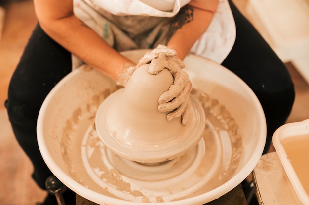 Free photo a potter works on creating a clay pot at her pottery wheel