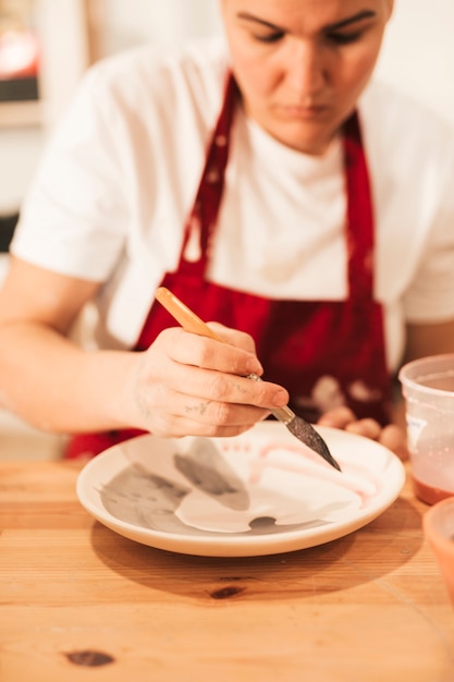 A pottery decorator painting a ceramic plate with paintbrush on wooden plate