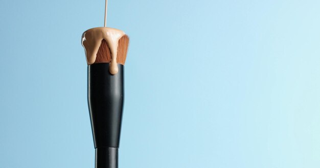 Pouring bb cream or foundation on the bristles of a professional make up brush with black handle isolated on blue