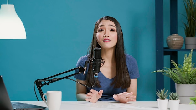 POV of asian woman filming live discussion on camera, recording podcast for online channel. Content creator chatting with audience and broadcasting vlog on social media. Tripod shot.