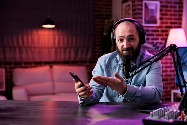 POV of content creator reviewing smartphone product on camera, filming podcast video in studio with neon lights. Online vlogger doing mobile phone recommendation on internet livestream.