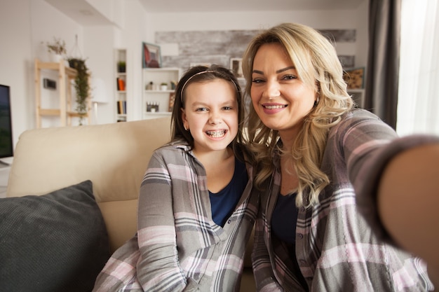 Free photo pov of of little girl with a big smile showing her braces with her mother sitting on the couch.