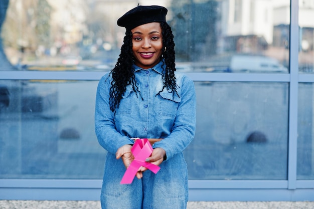 The power to fight Stylish fashionable african american women in jeans wear and black beret against modern building with pink ribbon for breast cancer