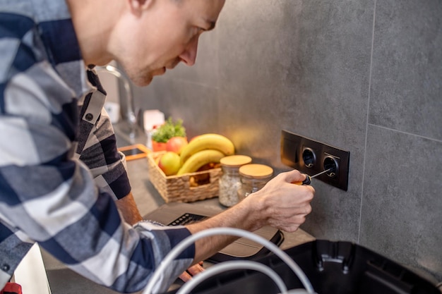 Free photo power socket closeup photo of man touching black socket on kitchen wall with special screwdriver