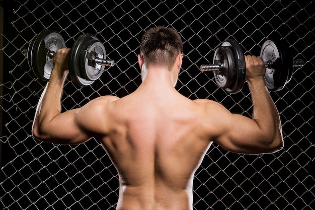 Free Photo powerful guy with a dumbbells showing muscles on fence  